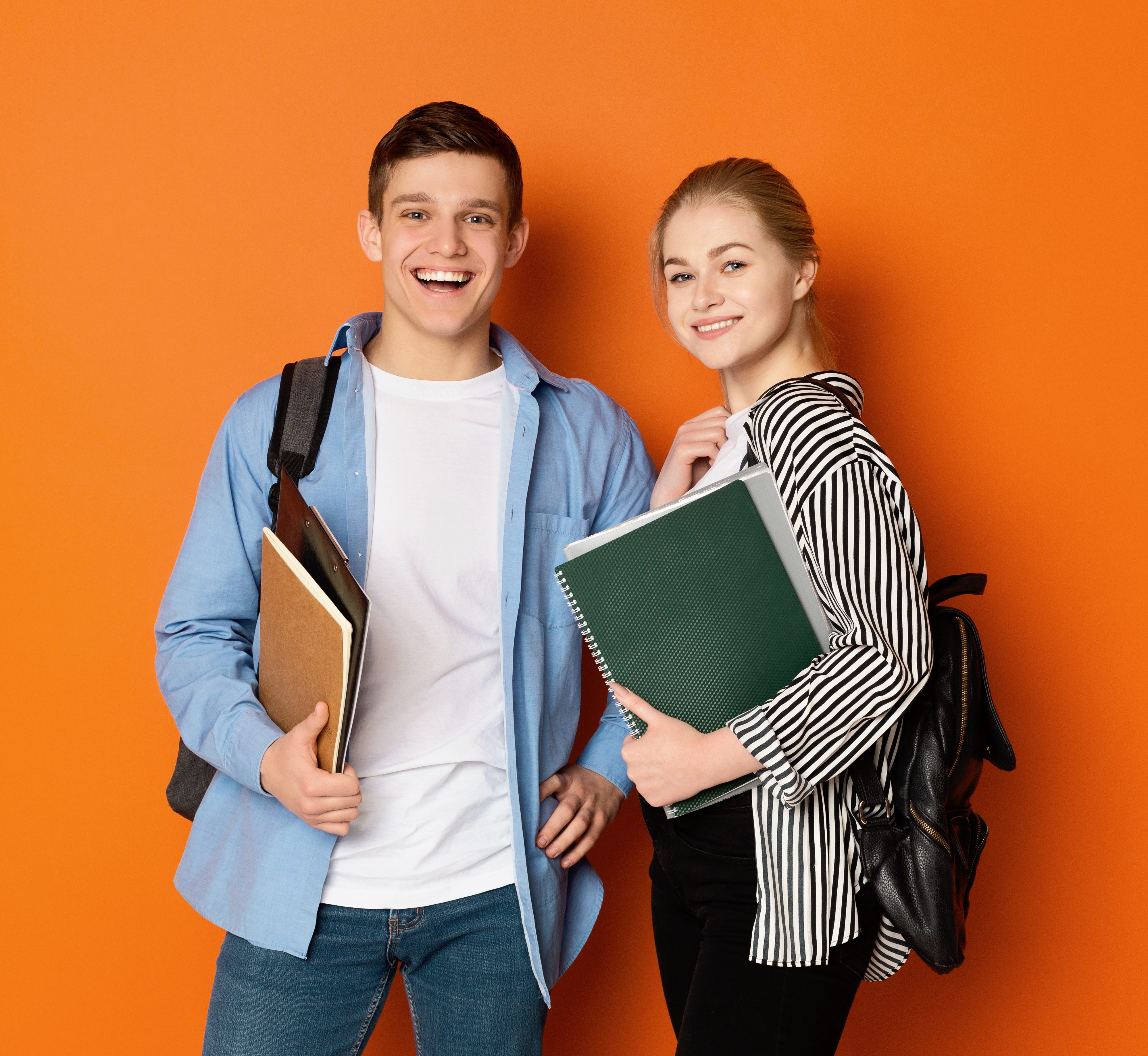 Excited student couple with backpacks and books