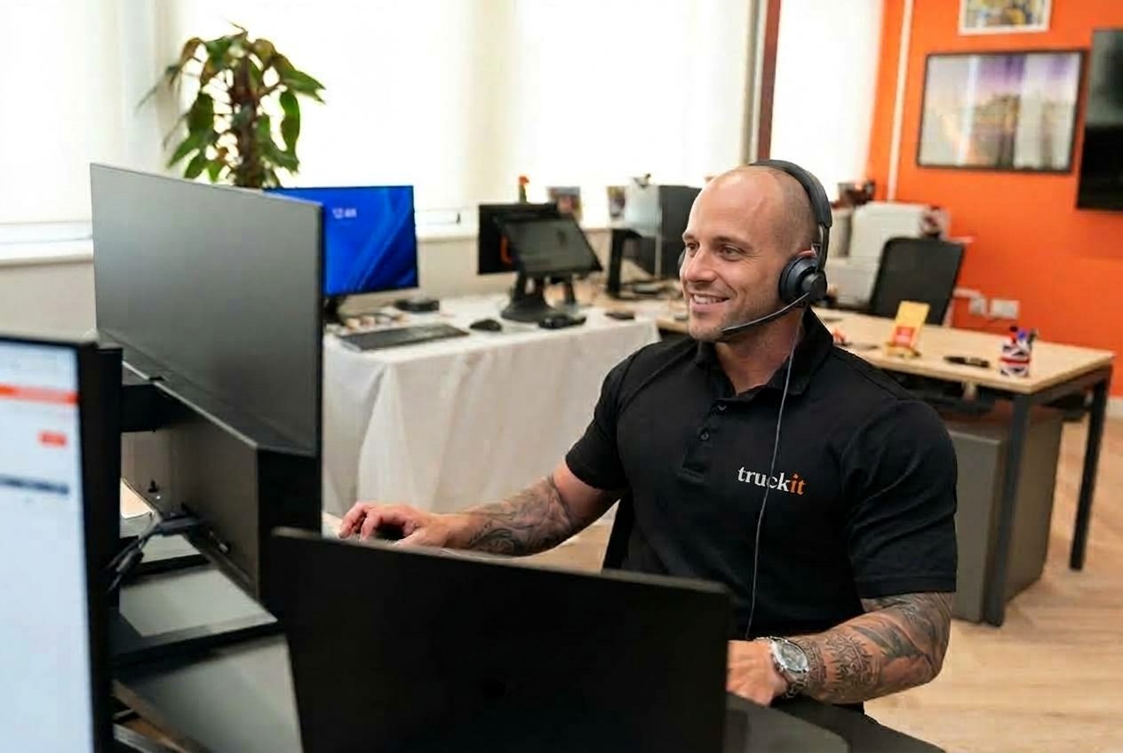 Medewerker van Truckit met headset en microfoon aan een bureau met beeldschermen, in een kantoor met oranje wand