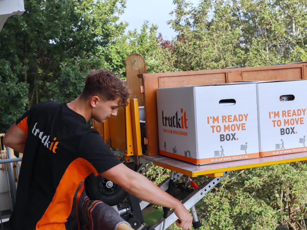 Verhuizer van Truckit bedient de verhuislift met verhuisdozen op het plateau