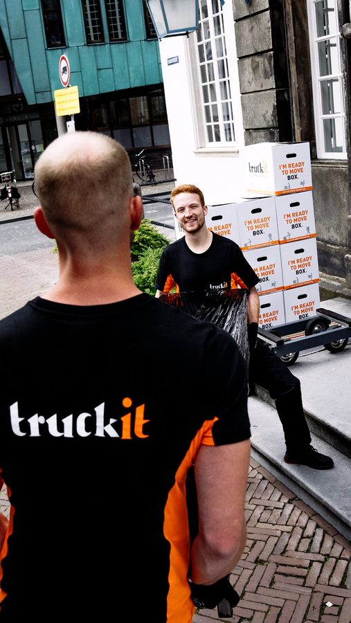 Verhuizer van Truckit lacht naar zijn collega bij een stapel dozen