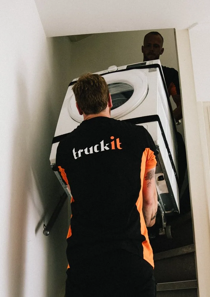 Verhuizer van Truckit draagt een wasmachine op zijn rug de trap op