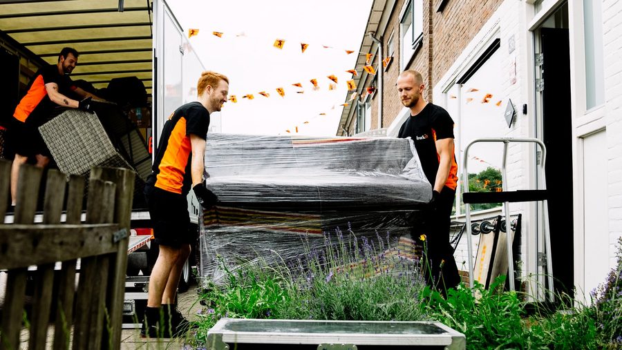 Drie verhuizers van Truckit dragen een bank door een voortuin