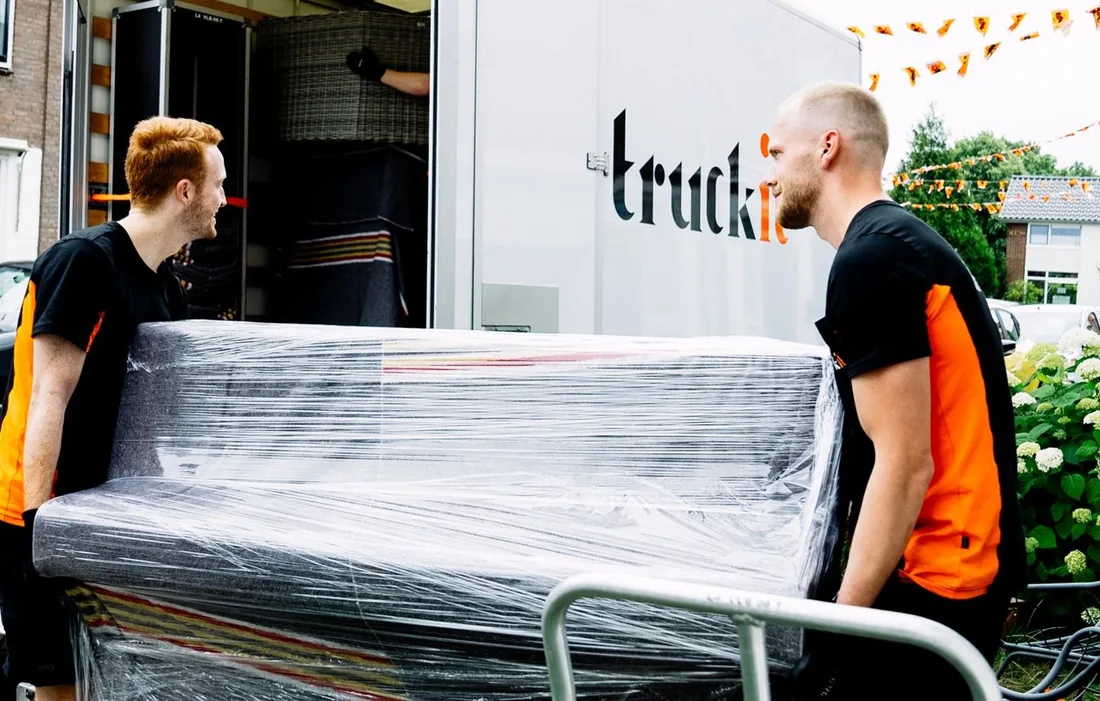 Twee verhuizers van Truckit dragen een ingepakte bank naar de verhuiswagen