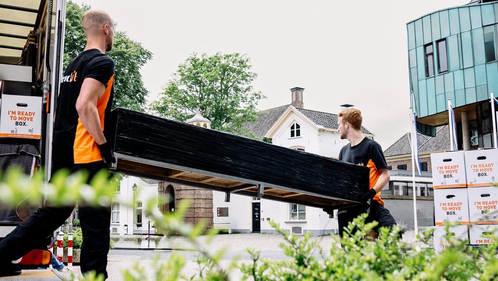 Twee verhuizers van Truckit dragen een bedbodem naar de wagen