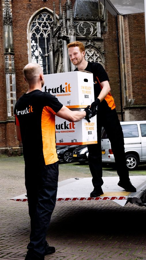 Twee verhuizers van Truckit geven verhuisdozen aan op de laadklep