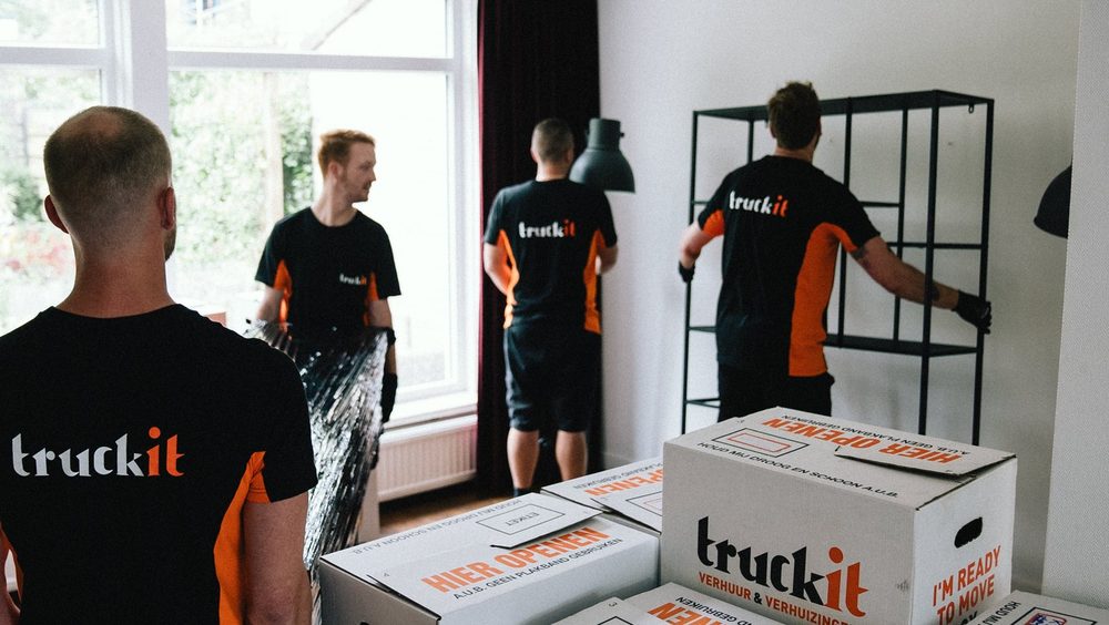 Vier verhuizers van Truckit zetten dozen en een kast neer in een lichte kamer