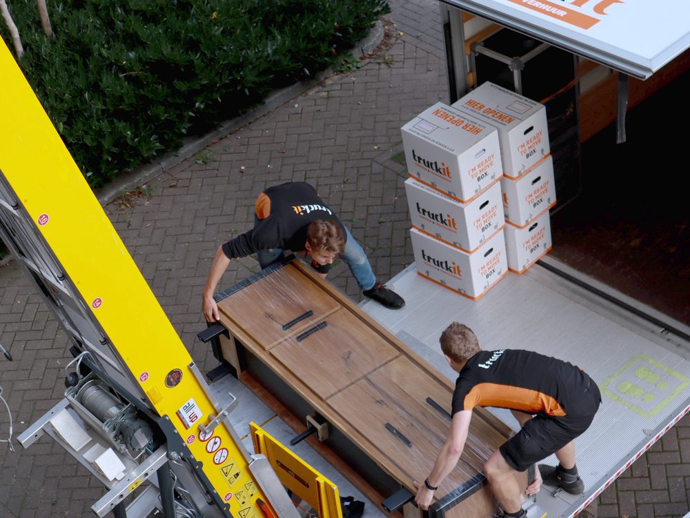 Twee verhuizers van Truckit leggen een kast op de verhuislift, van bovenaf gezien