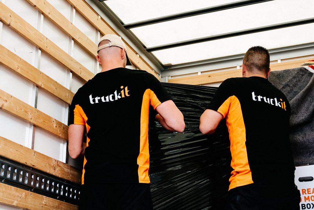 Twee verhuizers van Truckit zetten een ingepakt meubel vast in de laadbak