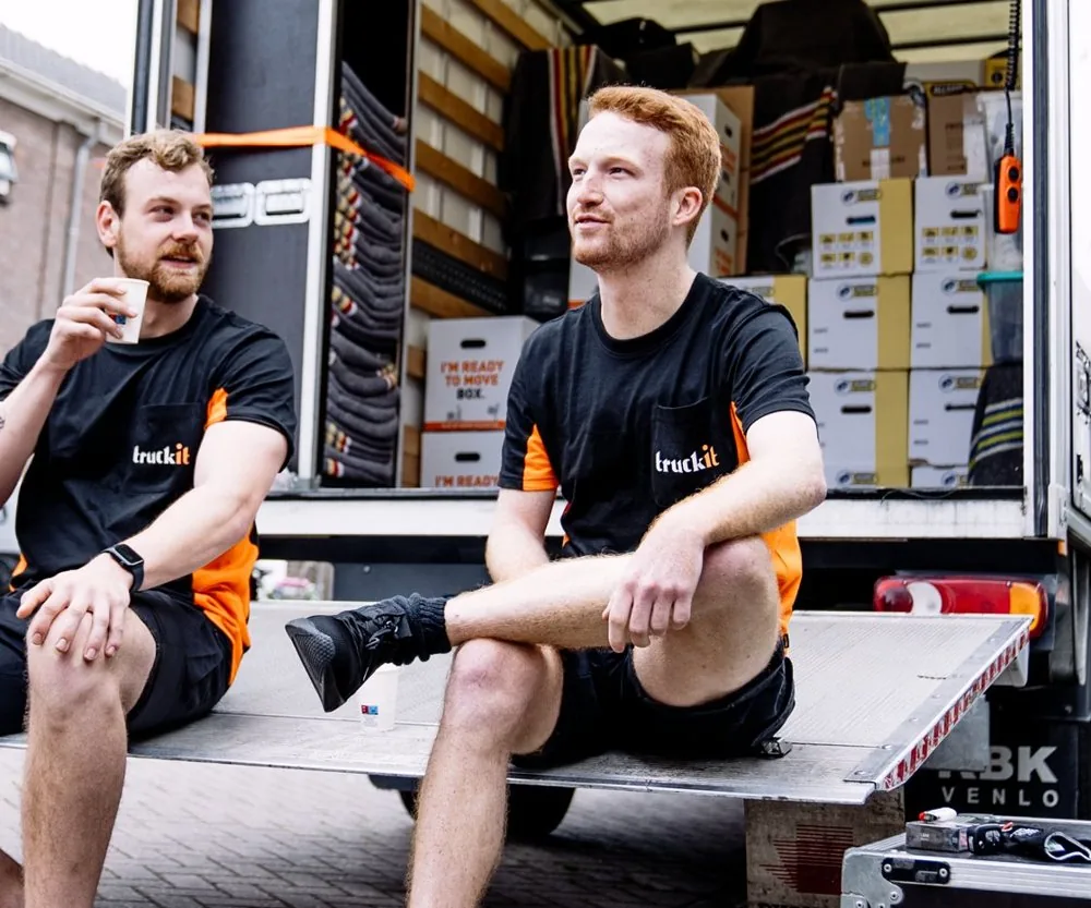 Twee verhuizers van Truckit nemen pauze op de laadklep van de verhuiswagen