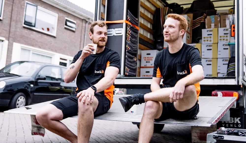 Twee verhuizers van Truckit op de laadklep van de verhuiswagen
