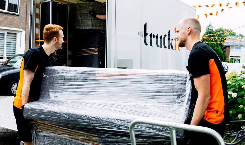 Twee verhuizers van Truckit rijden een ingepakte piano op de kar naar de verhuiswagen