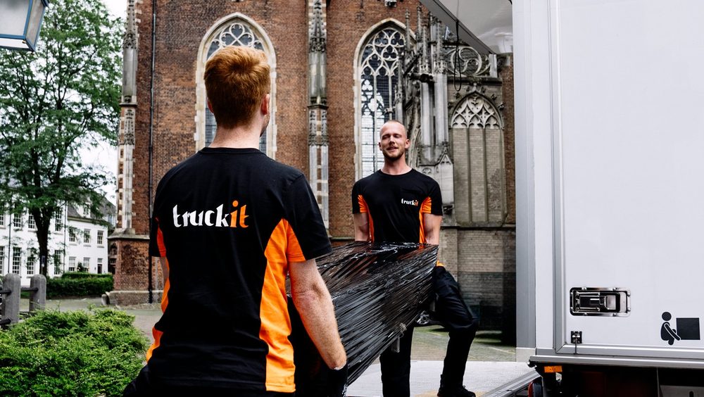 Twee verhuizers van Truckit dragen samen een ingepakt meubel naar de wagen