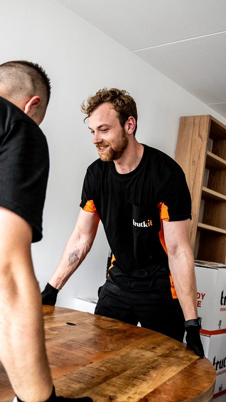 Verhuizer van Truckit tilt lachend een tafel met een collega