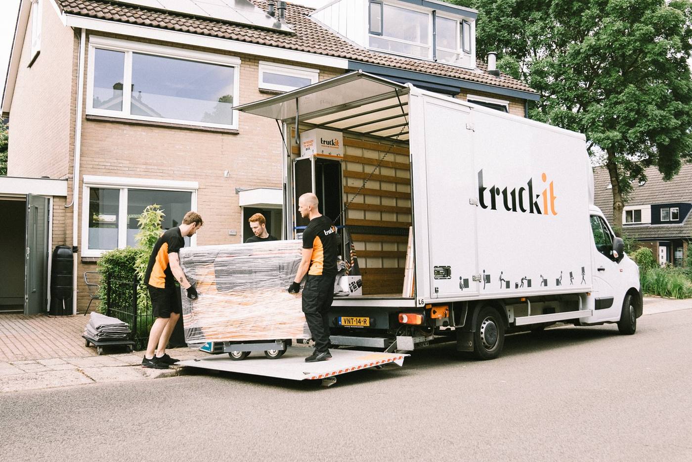 Drie verhuizers van Truckit rijden een ingepakt meubelstuk over de laadklep de verhuiswagen in