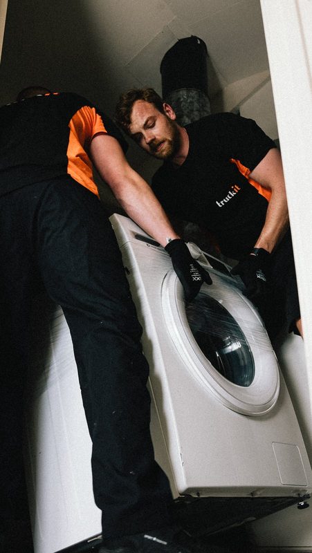 Twee verhuizers van Truckit tillen samen een wasmachine de trap af