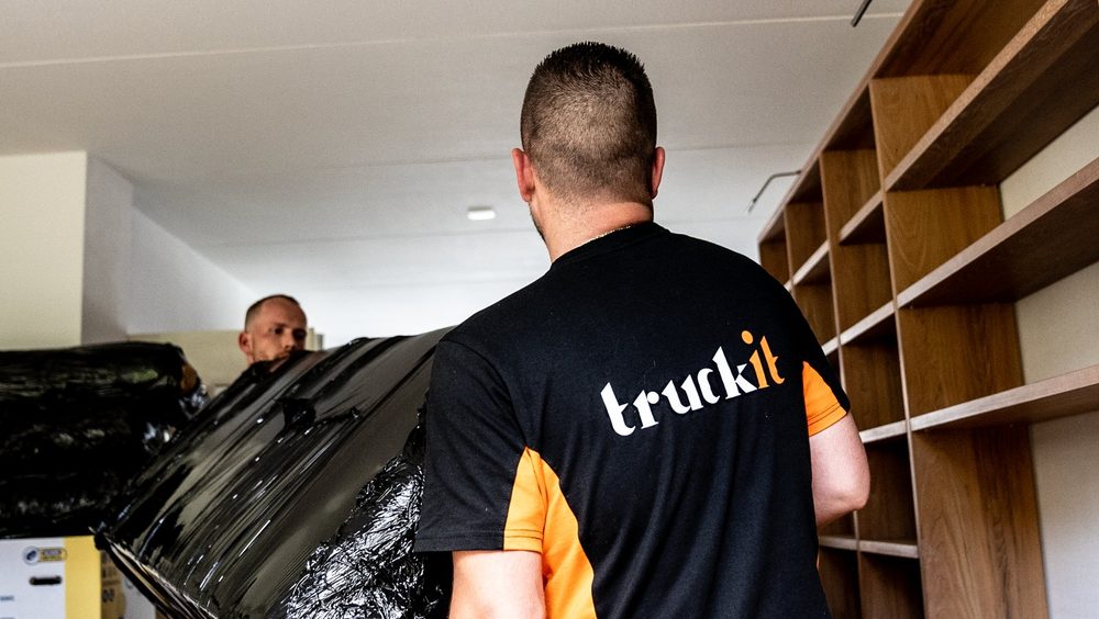 Twee verhuizers van Truckit dragen een ingepakt meubel door een lege kamer